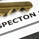Close-up image of a set of brass keys laying on top of a document titled "Home Inspection Checklist." The focus is on the keys and the title of the checklist.