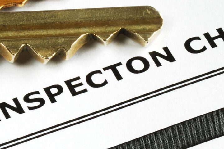Close-up image of a set of brass keys laying on top of a document titled "Home Inspection Checklist." The focus is on the keys and the title of the checklist.